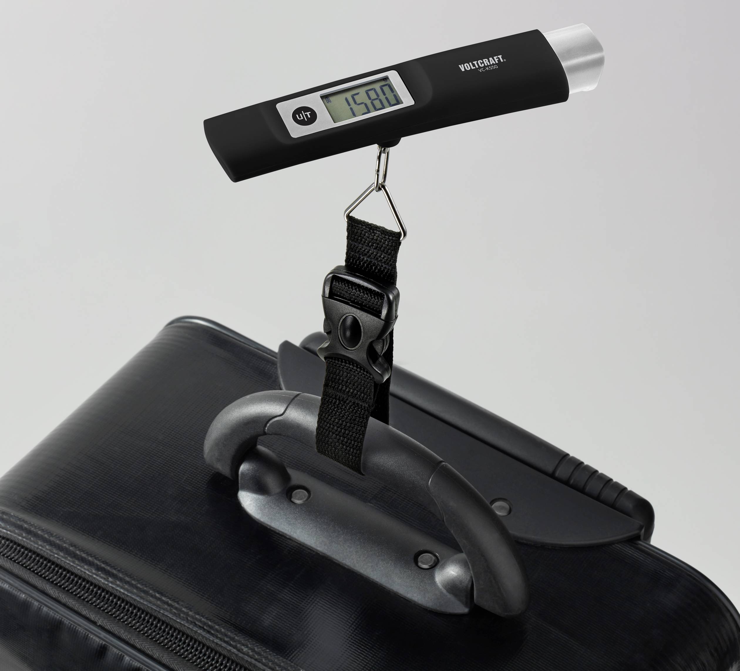 A digital luggage scale shows a weight of 15.80 kg while attached to a black suitcase handle.