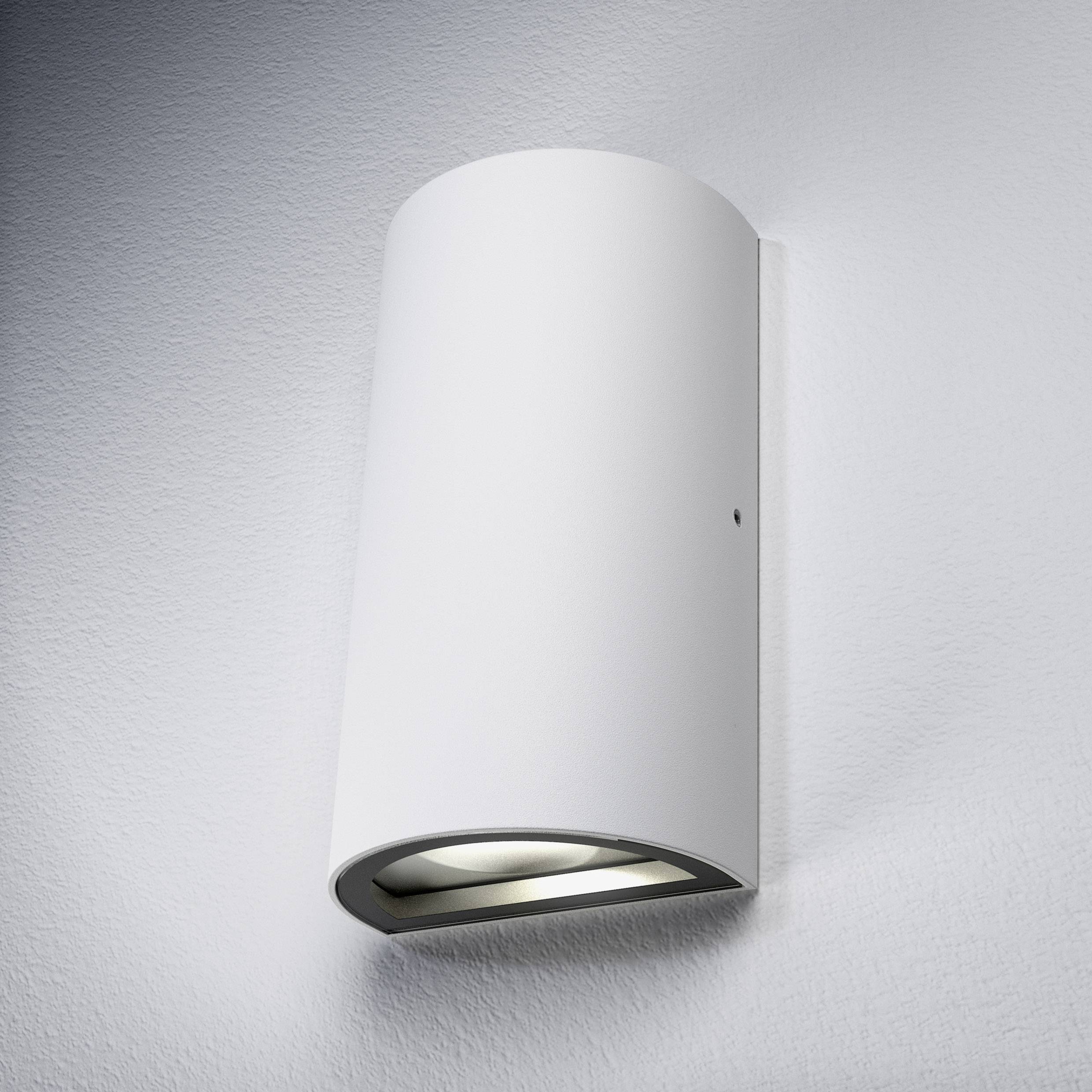 A contemporary, cylindrical metal wall light with downward-facing illumination, mounted on a white wall.