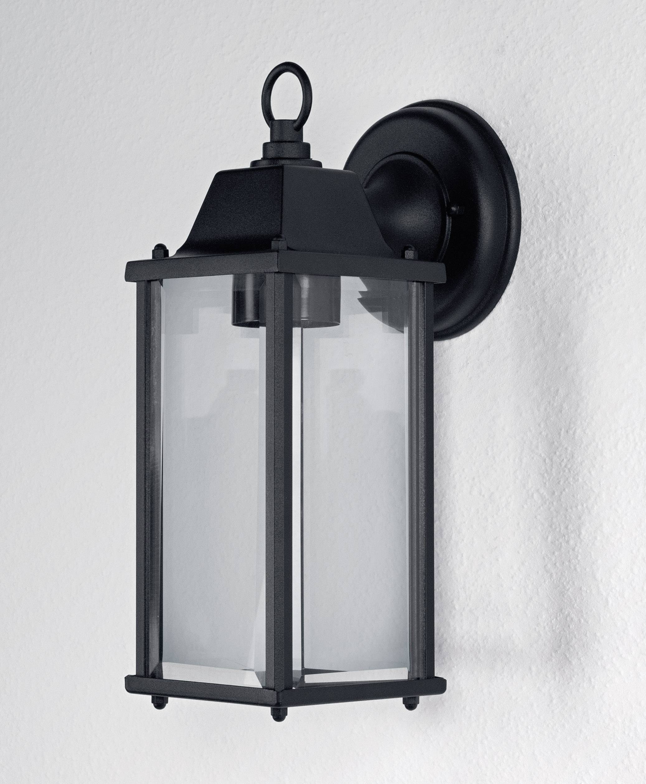 Black wall light made of metal and glass in a classic lantern style, mounted on a white wall.