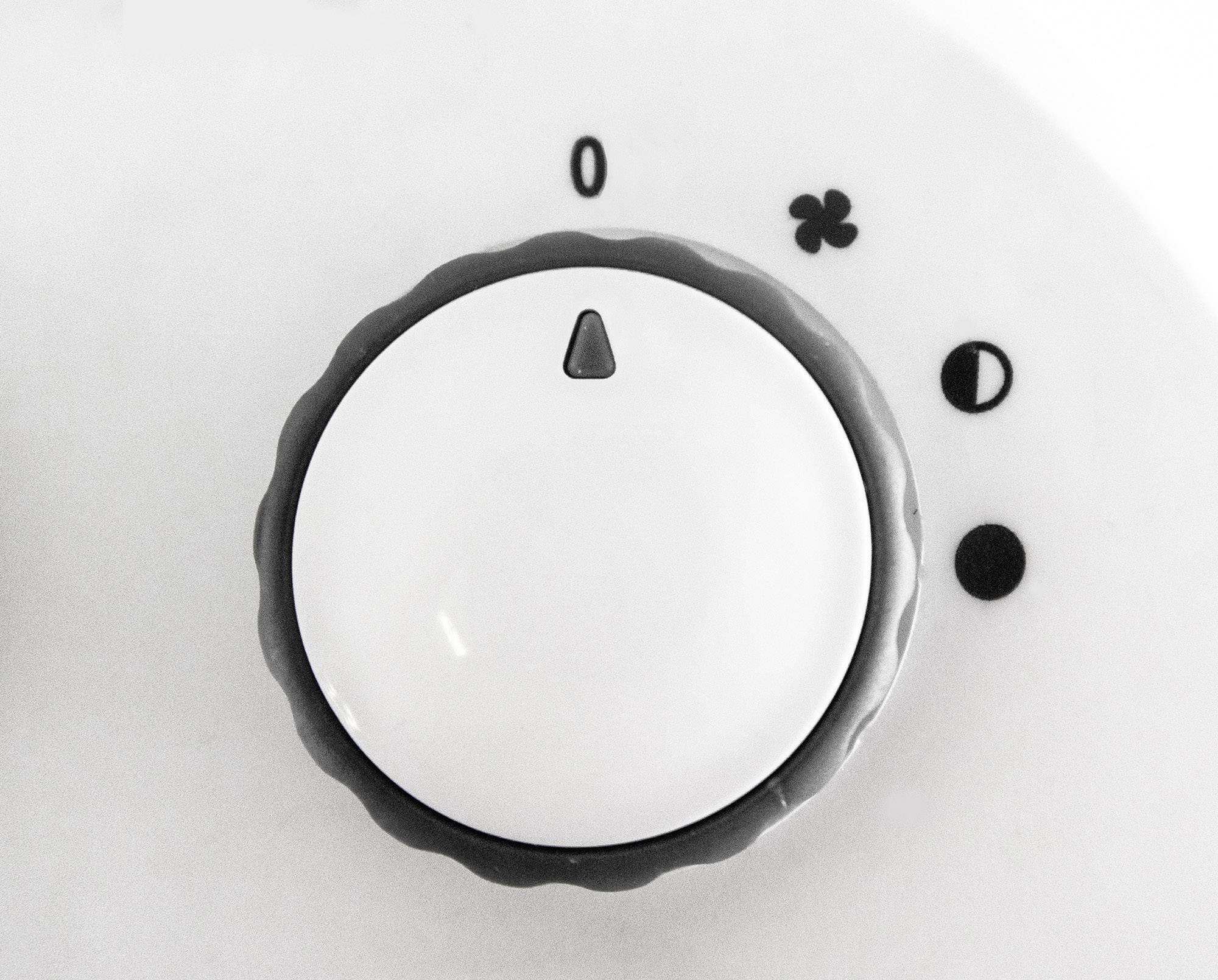 'Close-up of a white rotary switch with four symbols: Zero, Fan, Heating Level 1, Heating Level 2.'