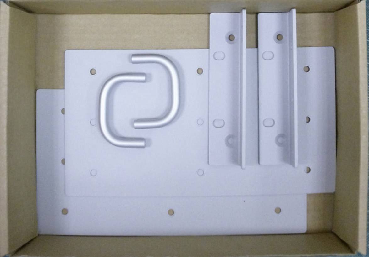 White metal plates and brackets in a cardboard box. The plates have holes for screws. A U-shaped metal handle lies on top.
