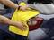 A person is cleaning the rear light of a car with a yellow cloth. Hands are visible on the cloth.
