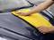 A person is wiping the bonnet of a car clean with a yellow cloth.