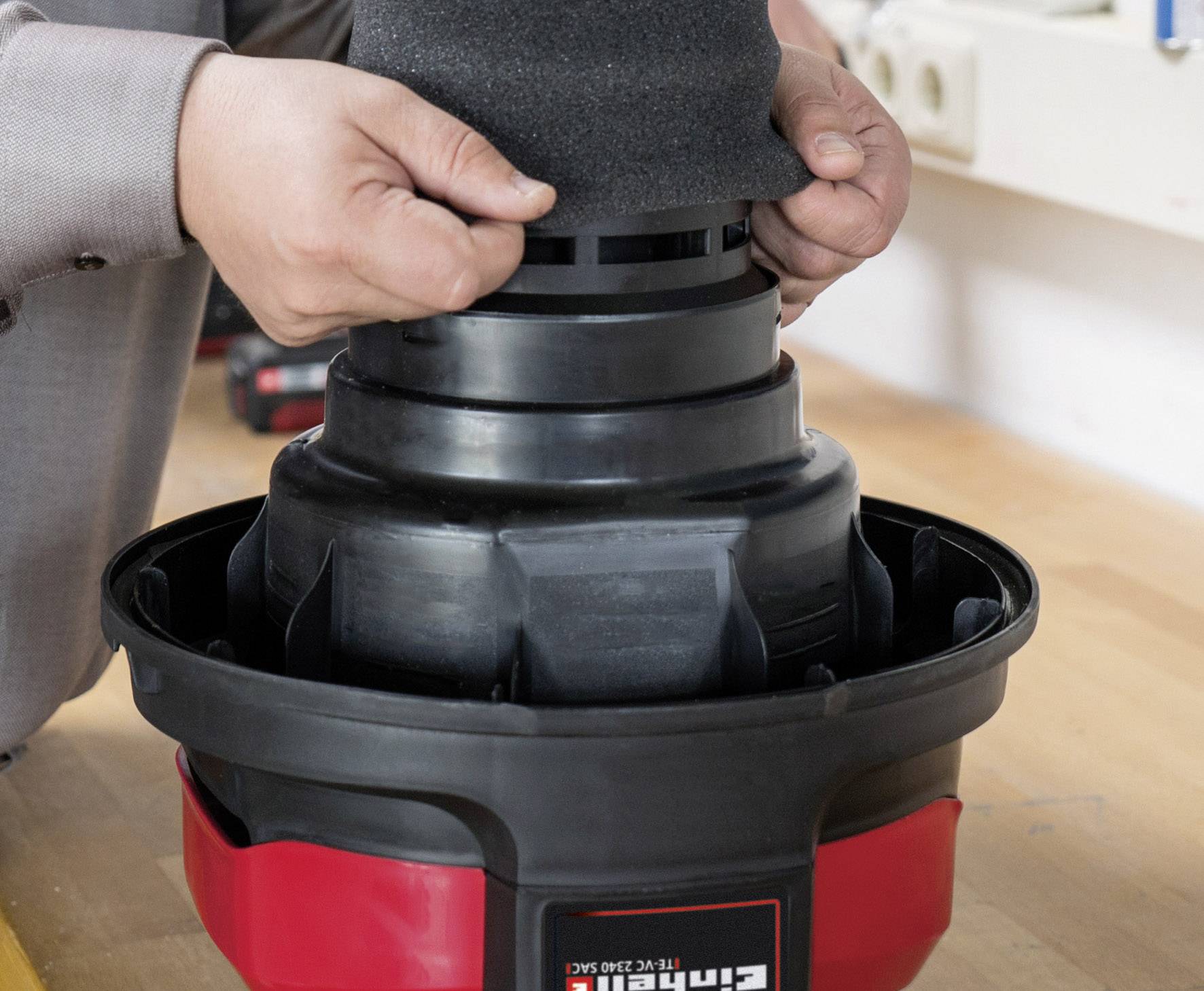 A person is installing a vacuum cleaner filter on a table in a workshop.