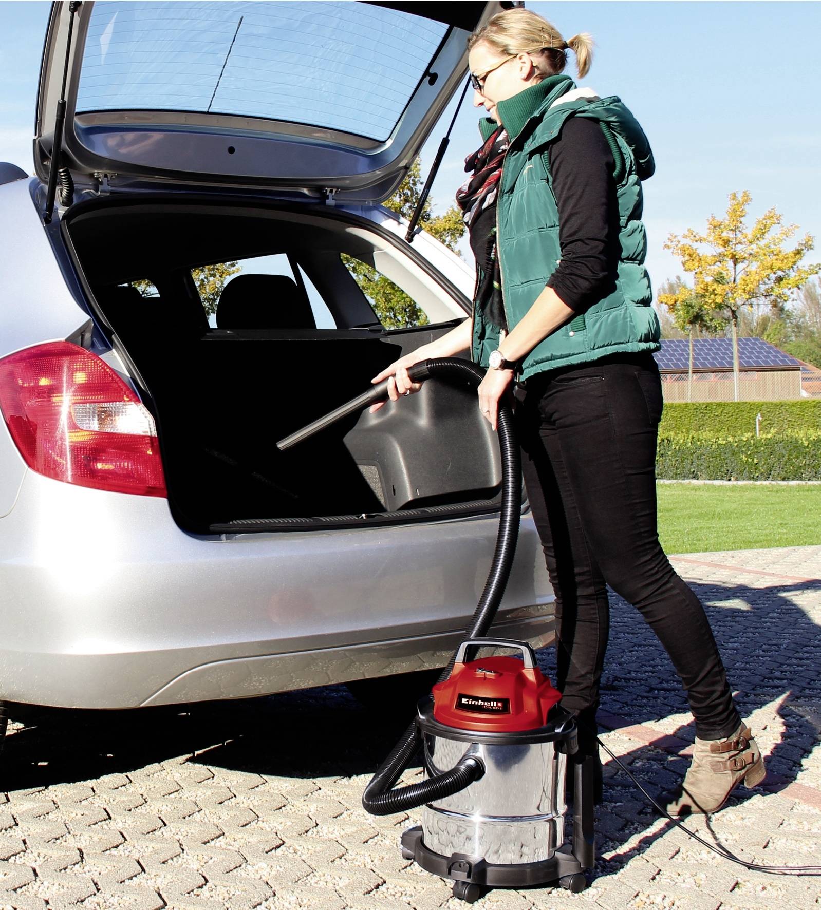 A woman is vacuuming the interior of a car boot in a car park using a vacuum cleaner.