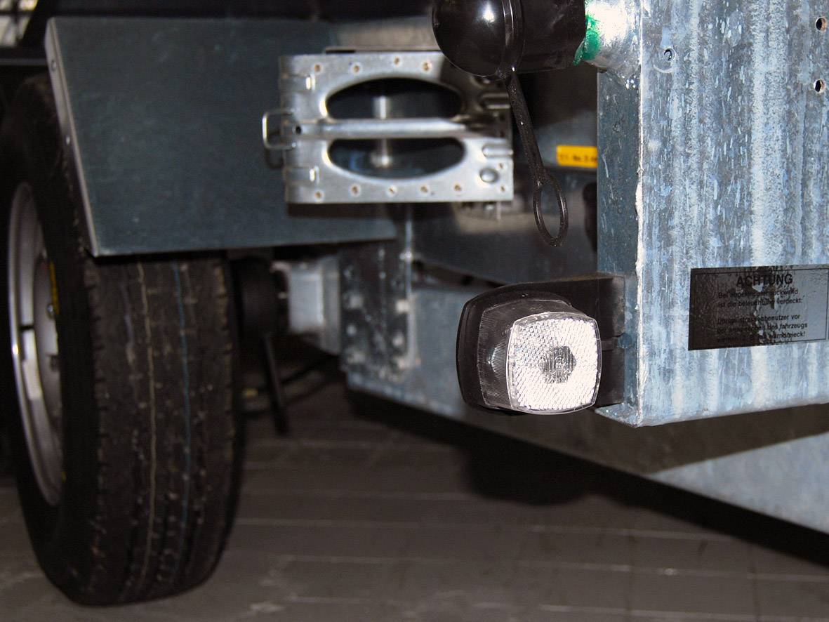 Trailer arm with reflector and wheel on an industrial floor.