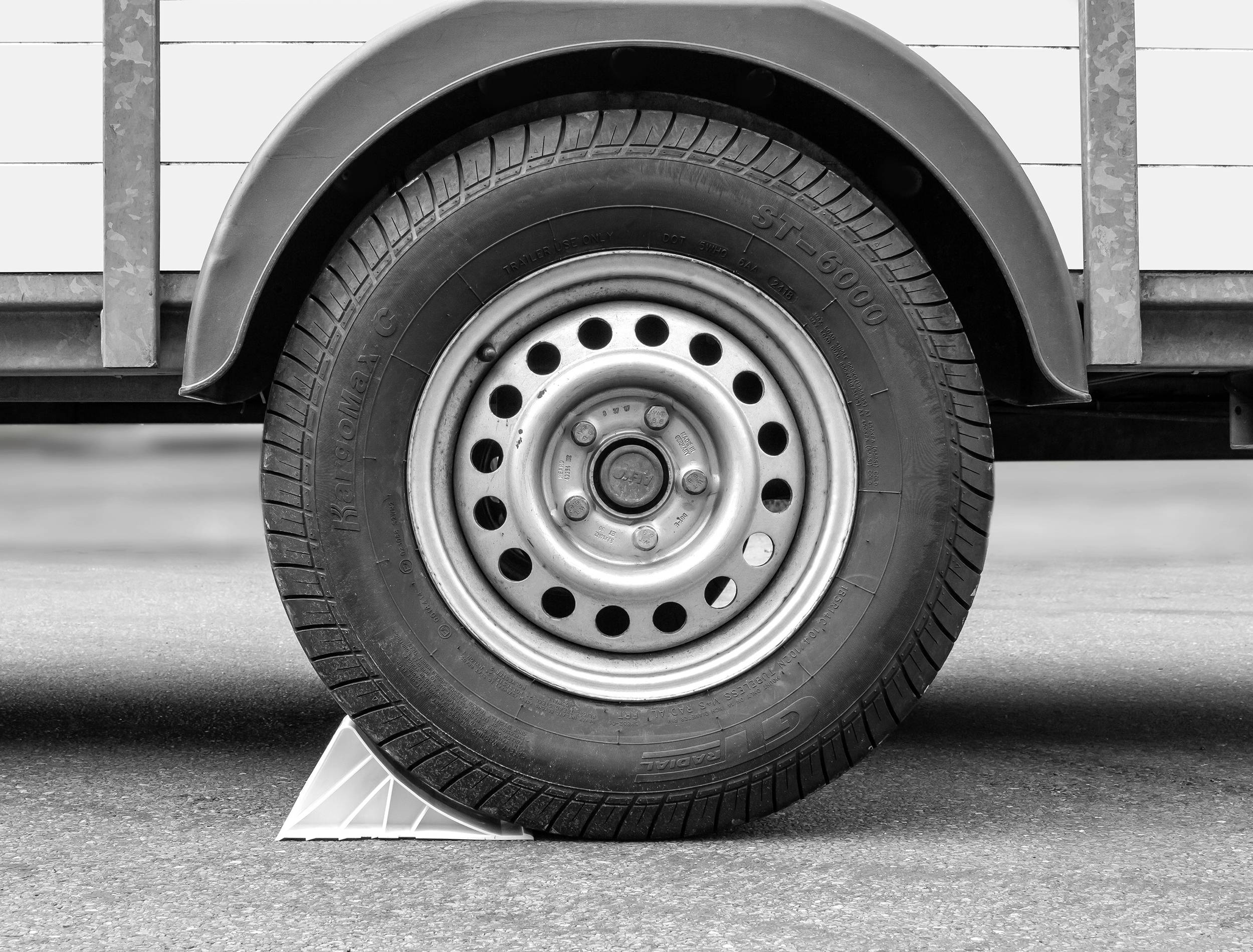 'Close-up of a trailer tyre secured by a white wheel chock to prevent rolling away.'