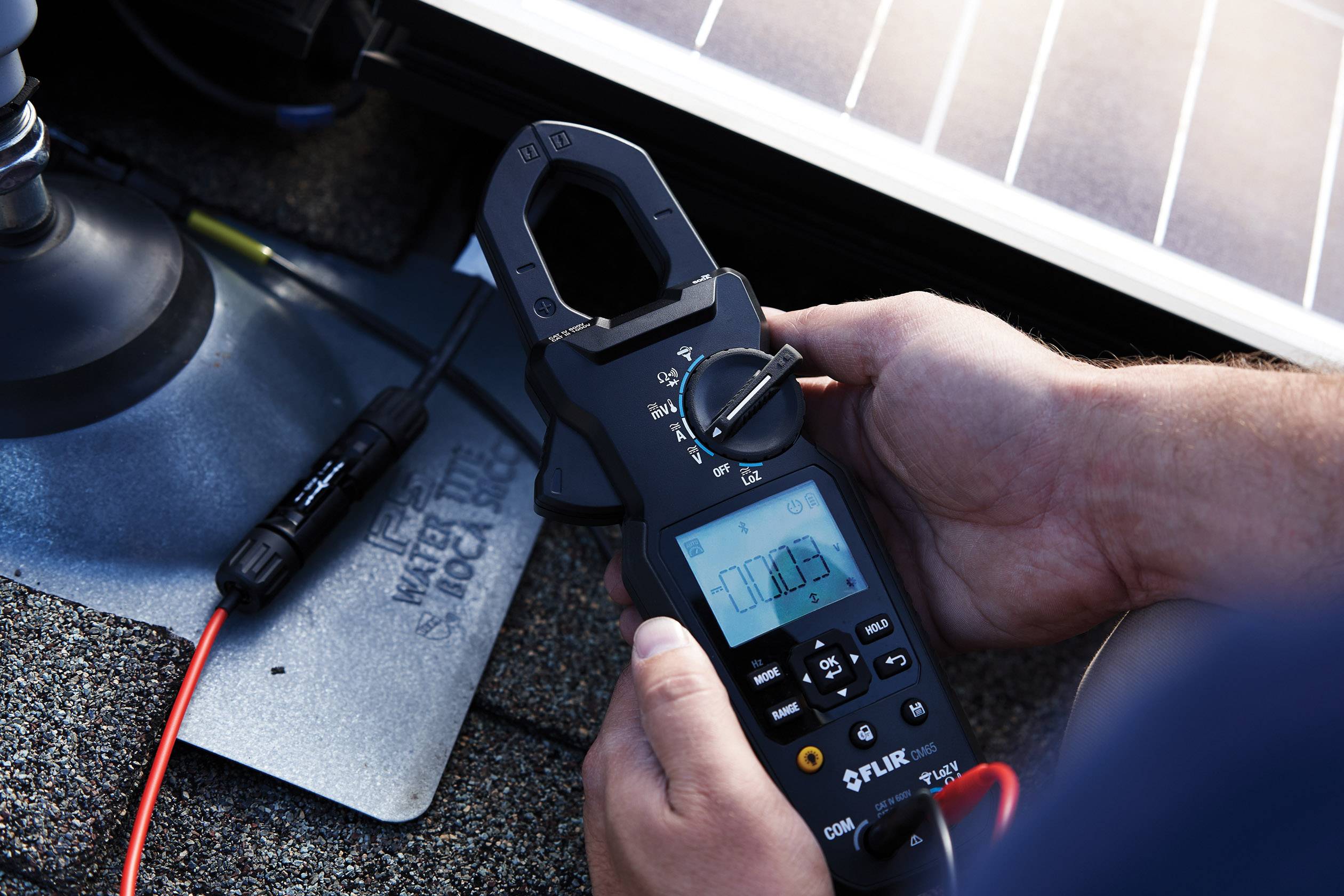 A person is measuring electrical voltage on a solar panel using a digital multimeter. The display shows '0.0003'.