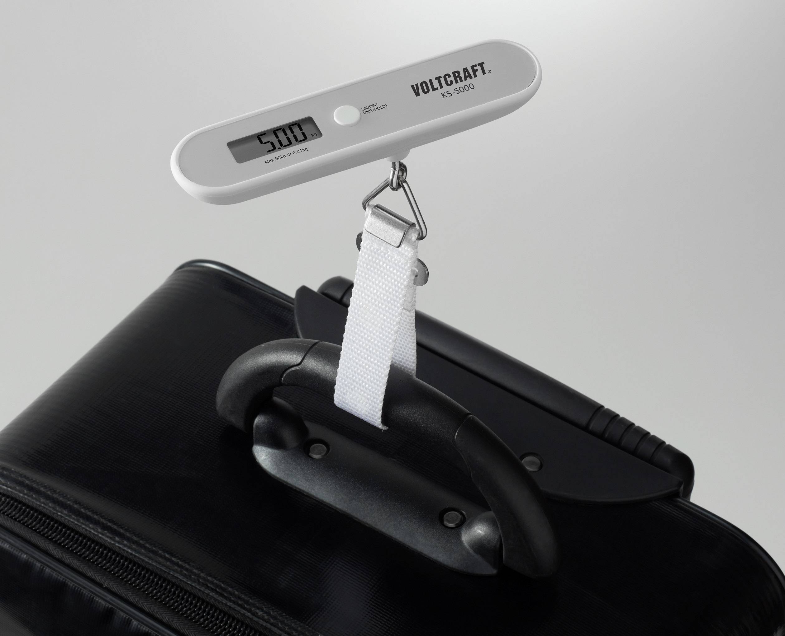 A digital luggage scales measures the weight of a black suitcase, attached to its handle. The display shows '5.00'.