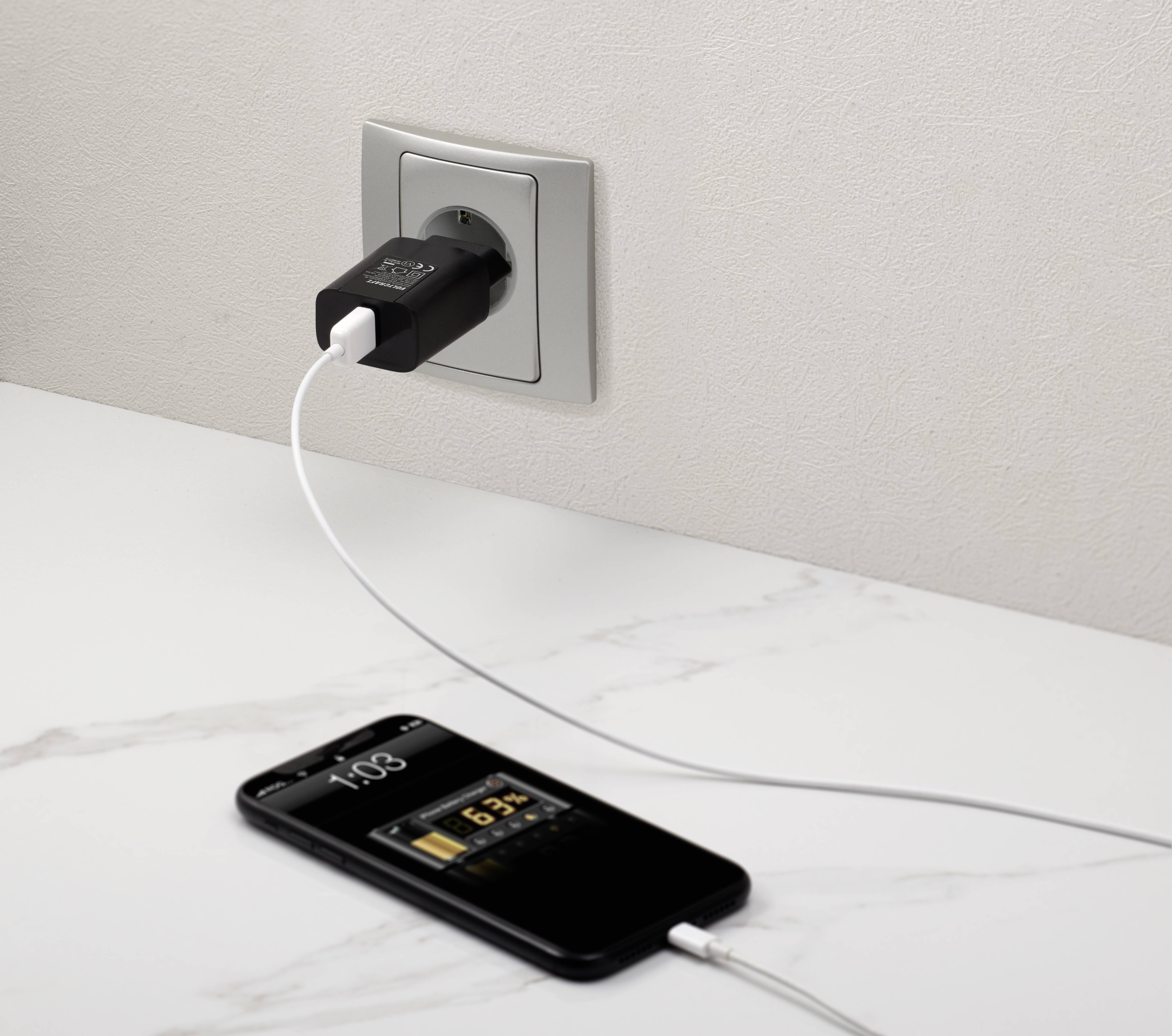 A smartphone is being charged via a USB cable at a plug socket. The display shows '65%' and the time.