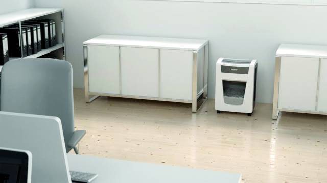 An office with filing cabinets, a shredder and a table with a laptop. Light wooden flooring and white walls.