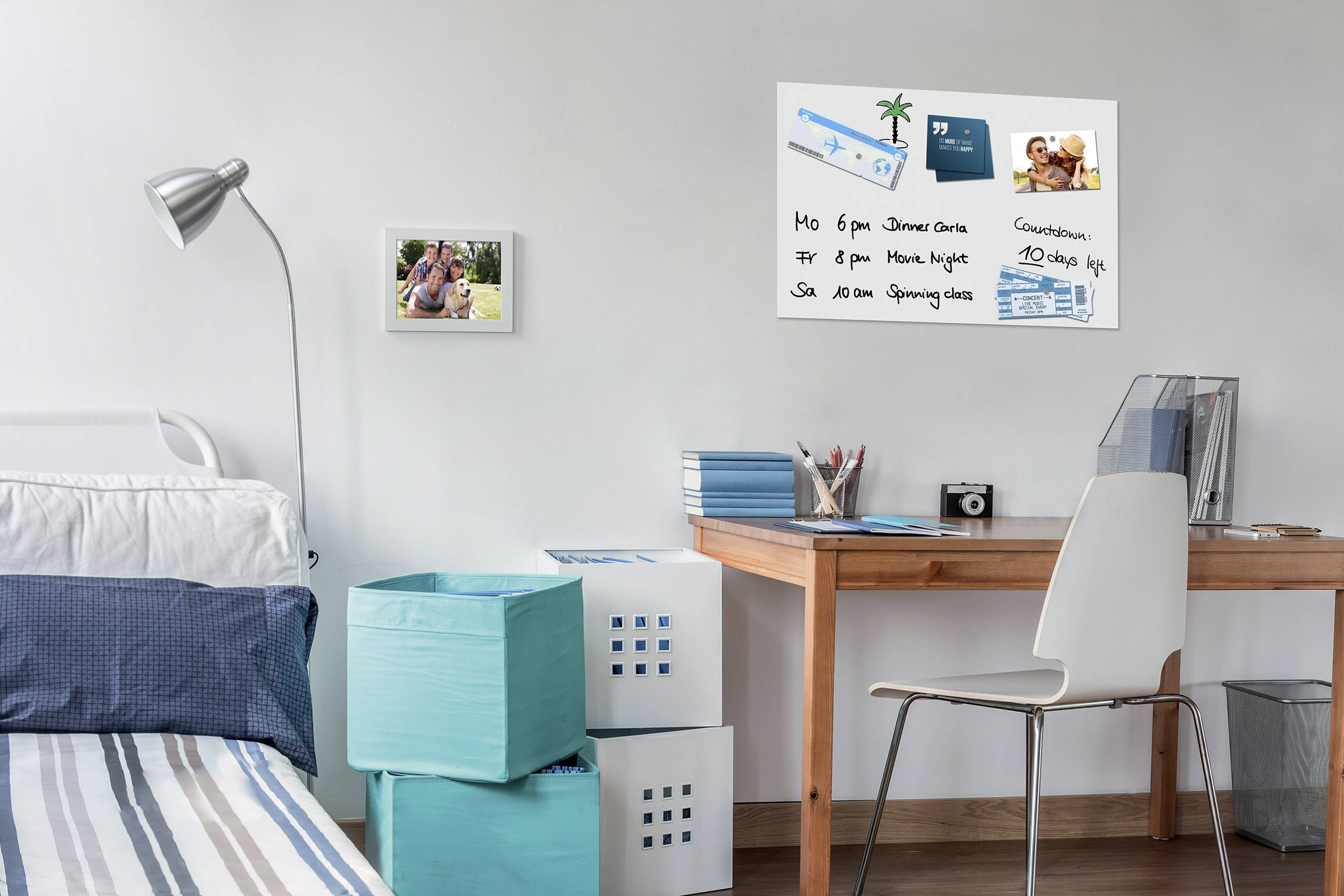 A bright bedroom with a desk, on which notebooks are lying. A pinboard with photos and notes is hanging on the wall.