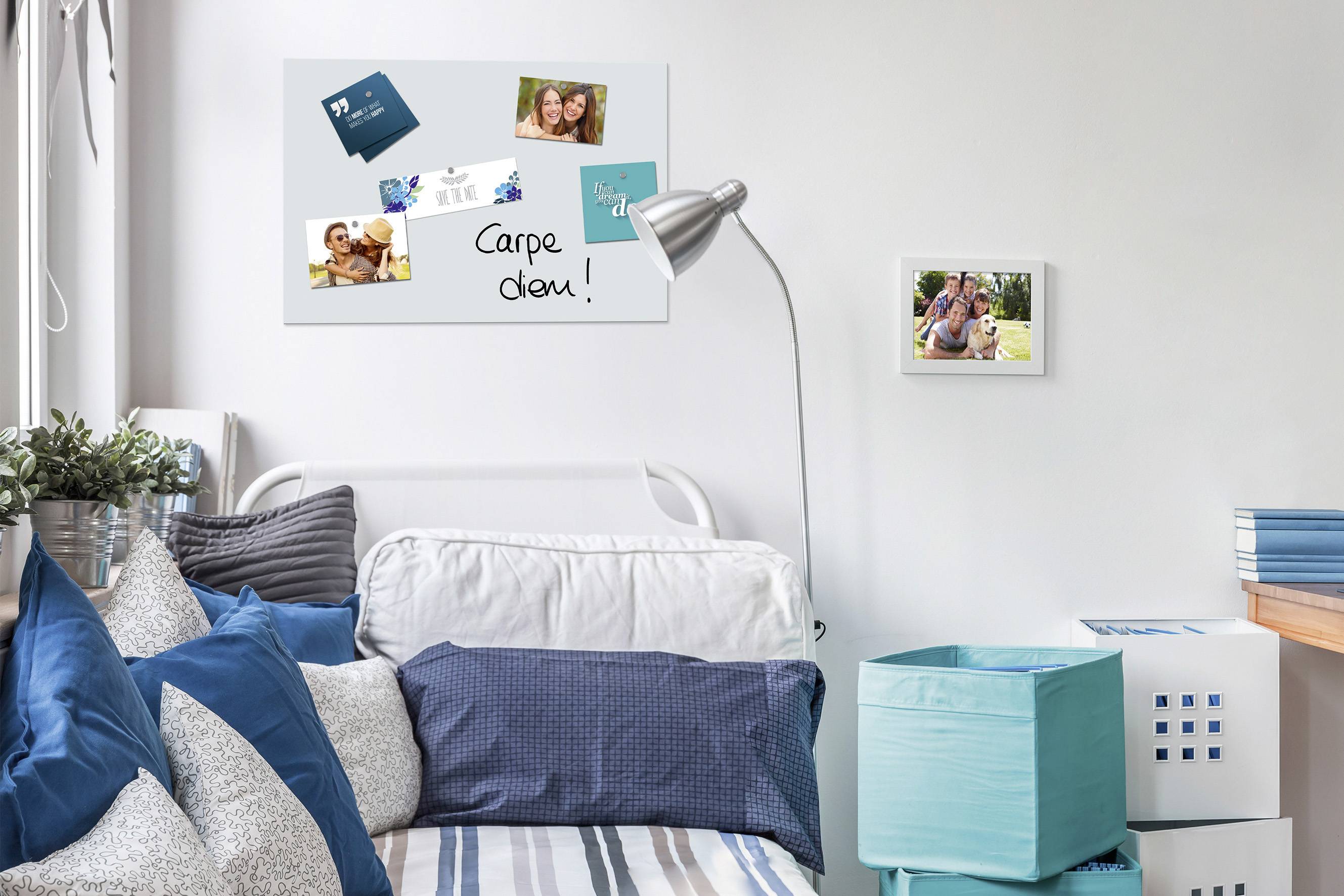 A cosy bedroom with a white bed, blue cushions and wall art. A desk lamp illuminates an inspiring quote: 'Carpe diem!'.