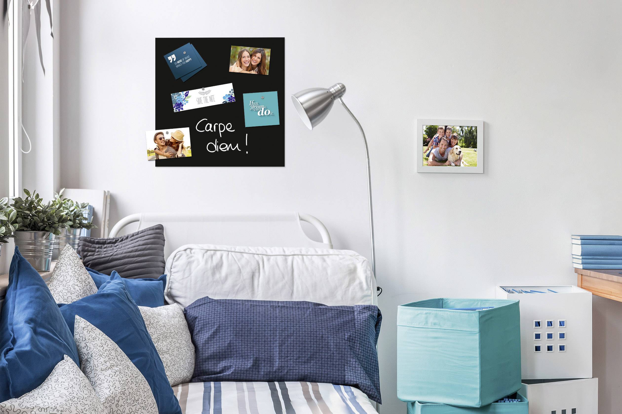 A modern bedroom with a white day bed, decorated with blue cushions. On the wall hangs a black pinboard with photographs and the inscription 'Carpe diem!'.