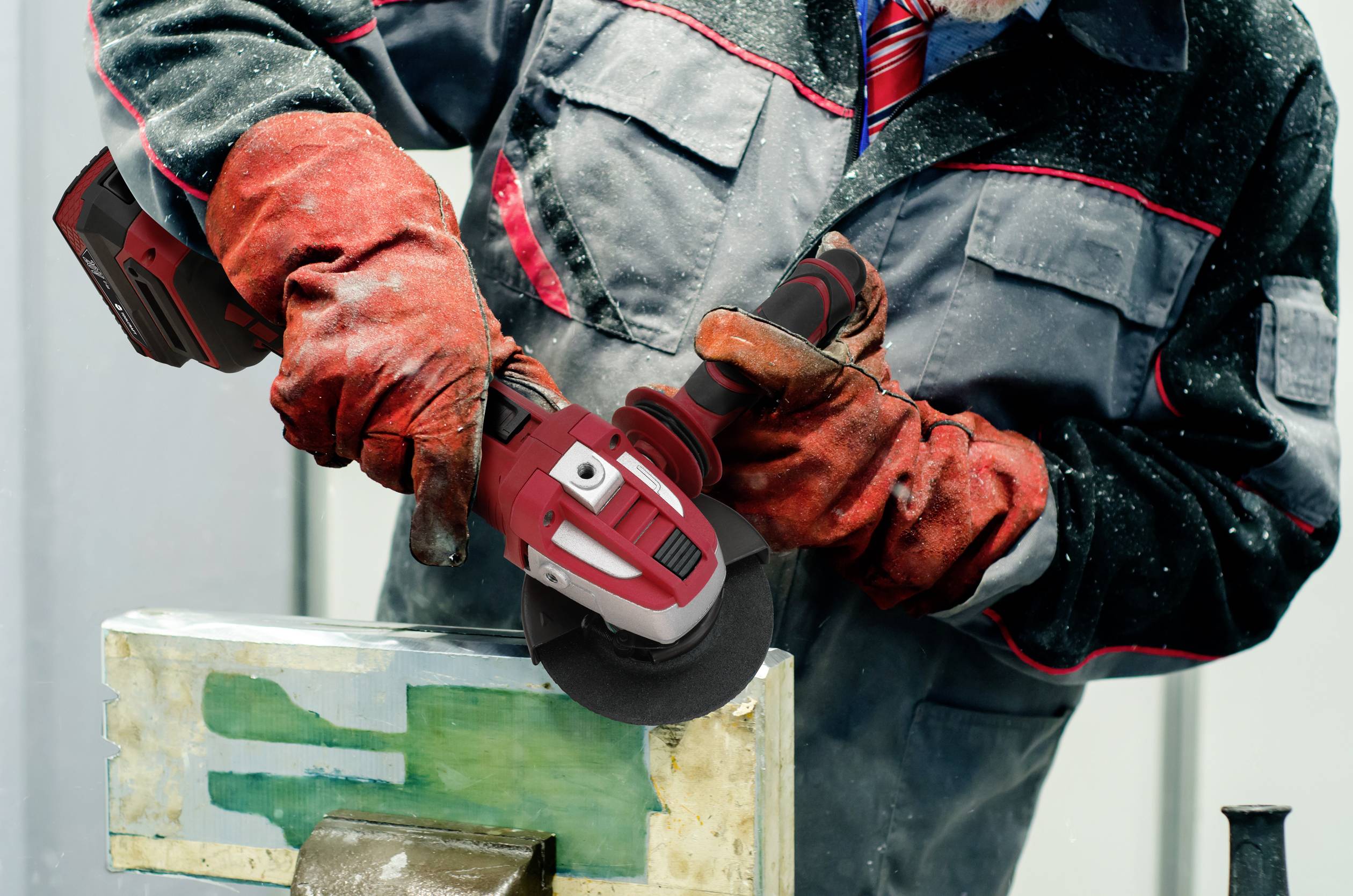 A worker in protective clothing is grinding metal with an angle grinder in a workshop.