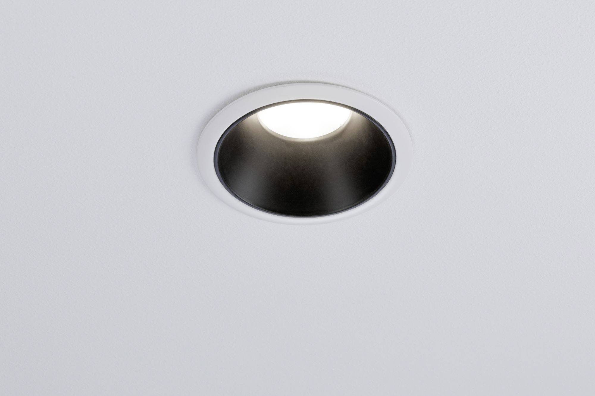 A round ceiling light, fitted into a white ceiling, shines brightly.