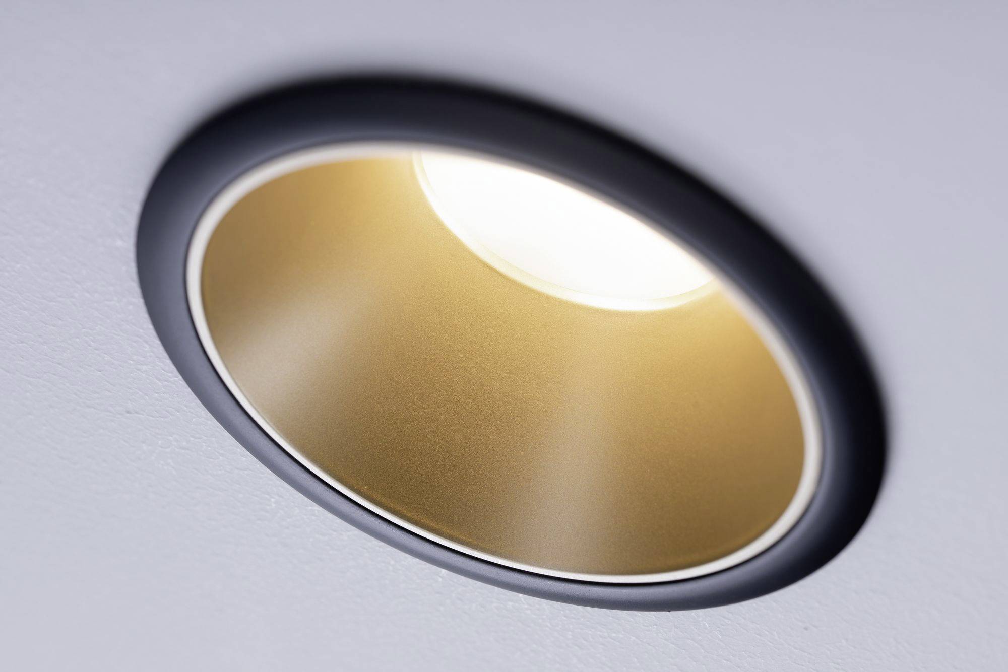 A round, recessed ceiling light with a golden reflector, emitting a warm light.