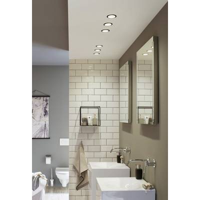 Bathroom with white tiles, two wash basins, mirrors and dark walls. Ceiling spotlights illuminate the room. A toilet is located in the background.