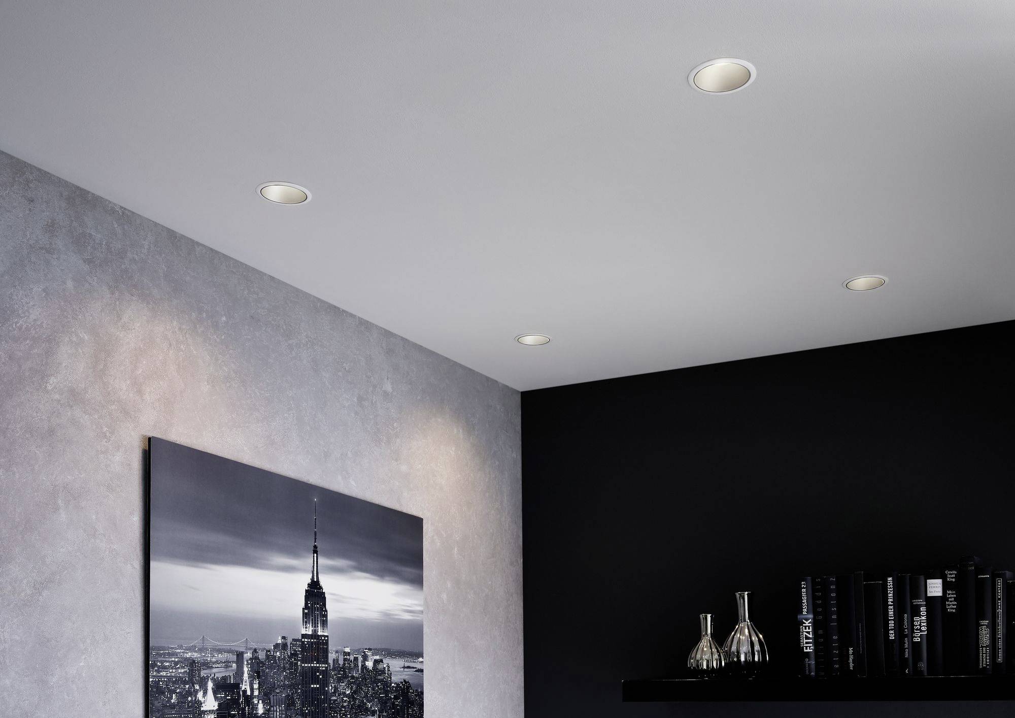 A modern space with recessed spotlights in the ceiling, a black and white picture of the Empire State Building on the wall and black shelves.