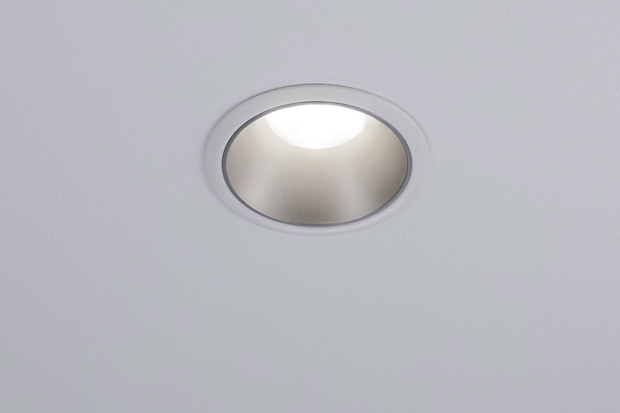 A round ceiling light emits a warm, white light. The light is recessed into a smooth, white ceiling.