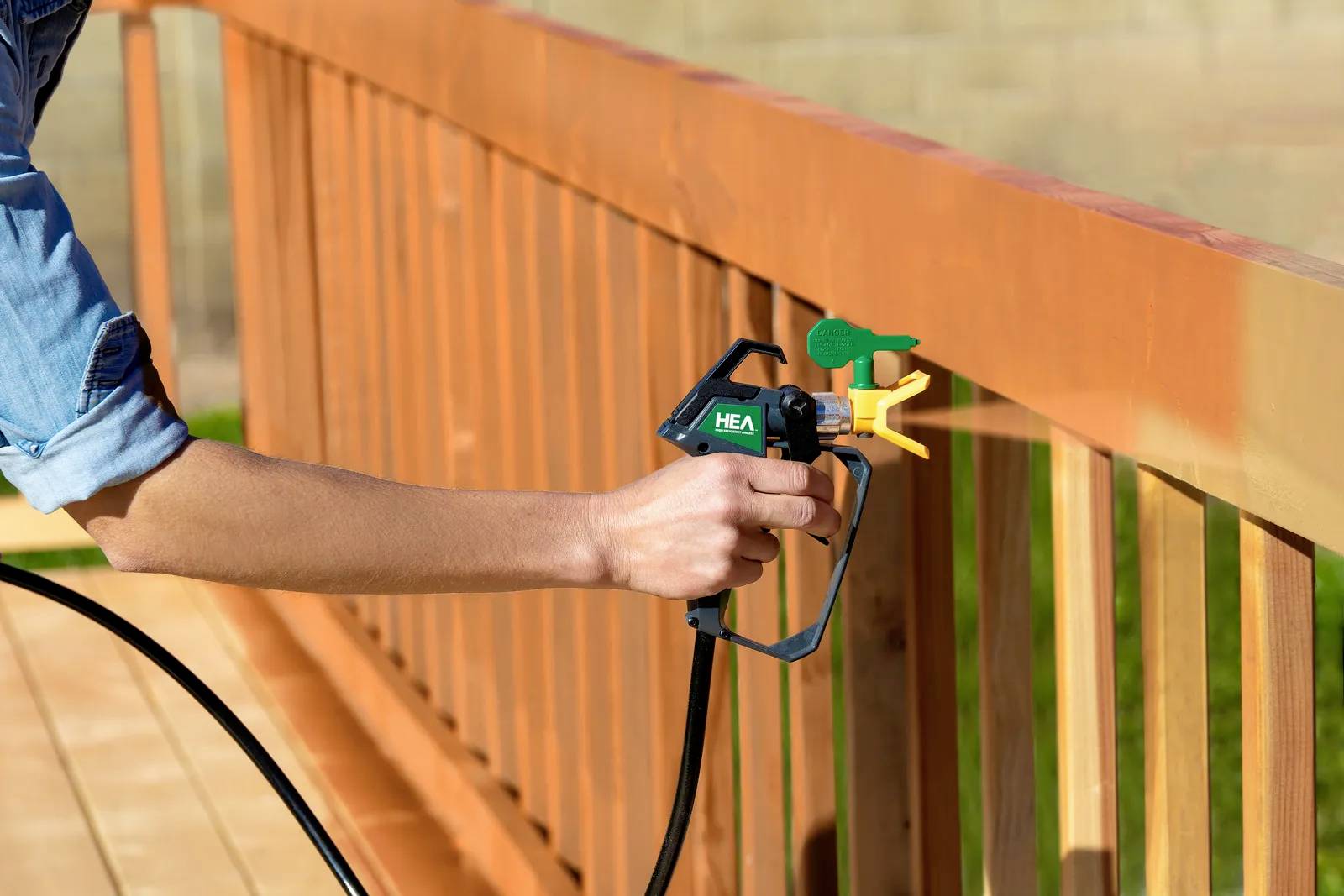 A person is spraying orange paint onto a wooden banister using a paint sprayer. Close-up of the arm and spraying device. Fresh paint is being applied.