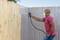 A man wearing a respiratory mask is spraying paint onto a wooden fence.
