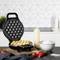 A waffle iron is baking egg waffles, surrounded by strawberries, a bowl of flour, and a squeeze bottle of batter in a modern kitchen.
