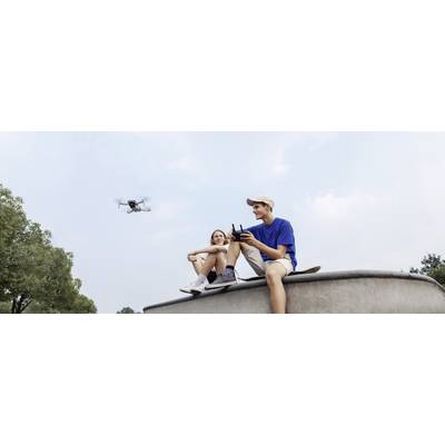 A woman and a man are jointly operating a drone in the park. They are smiling and sitting on an elevated platform outdoors.