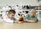 Two children in the laboratory are curiously examining a microscope on a table, surrounded by bottles and laboratory equipment in the background.