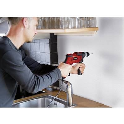 A man is drilling a hole in the wall above a kitchen sink using a red drill.