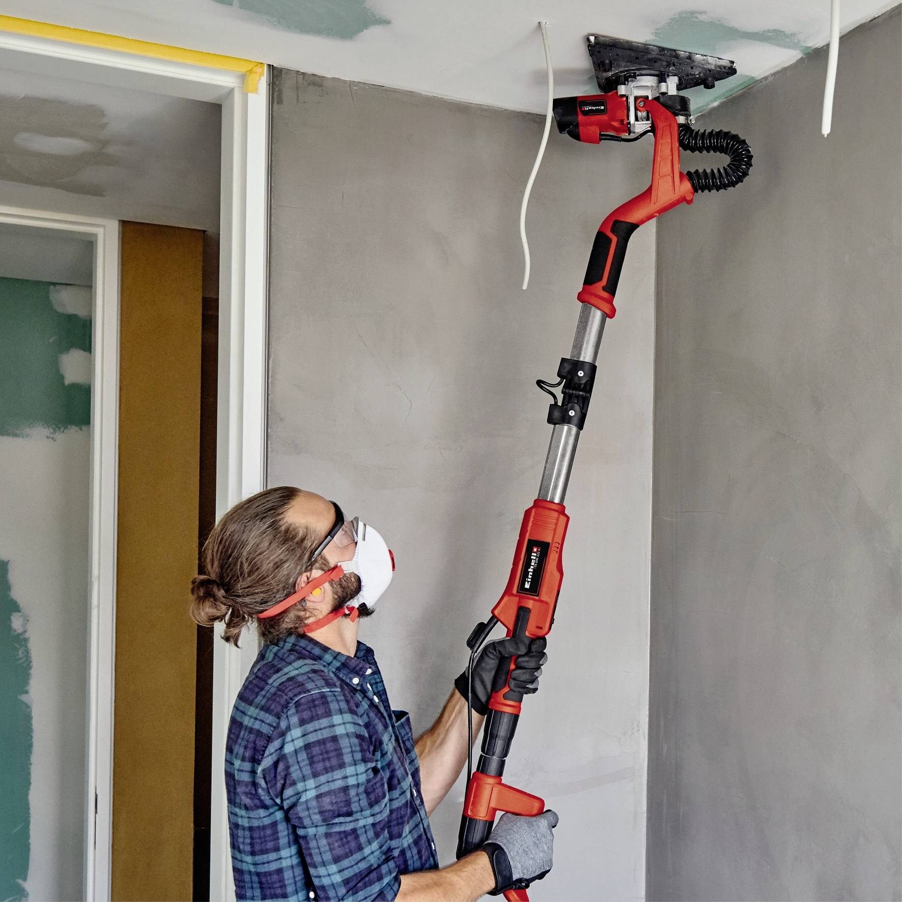 A person is sanding the ceiling with an electric sanding tool. They are wearing safety glasses and a dust mask to avoid dust.