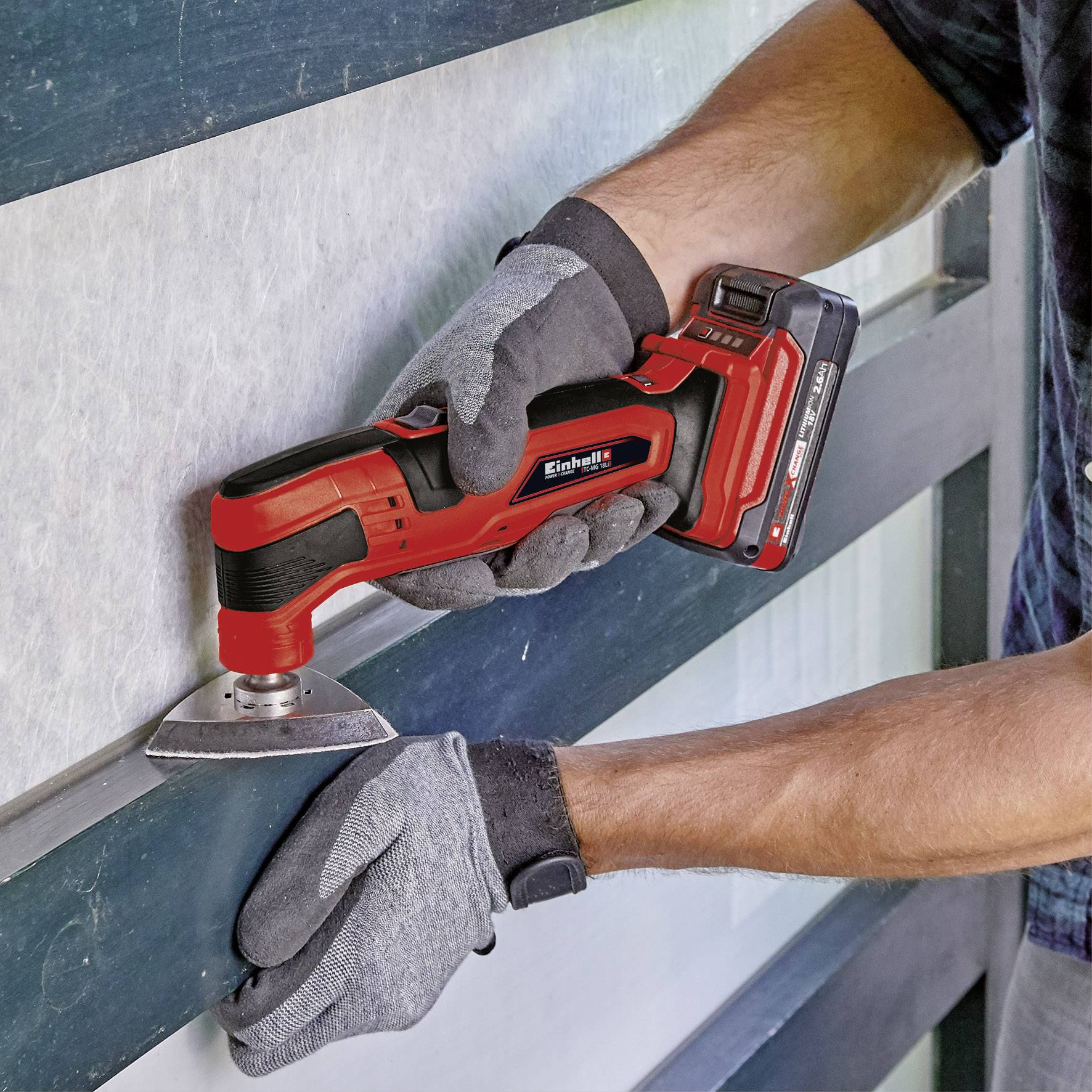 A person is using a red electric multi-tool to work on a metallic surface.