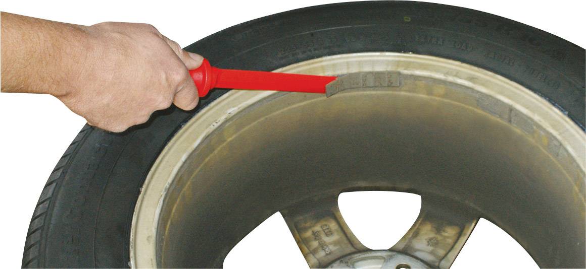 A tyre with a gauge checking the tread depth. A hand is holding the gauge against the tyre.