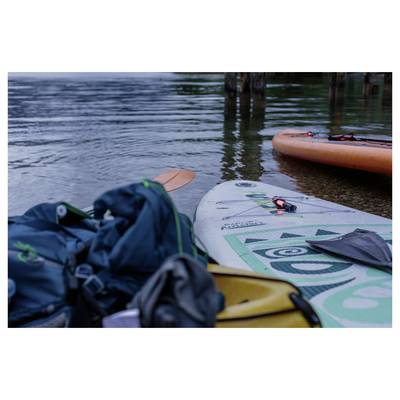 Stand-up paddleboards with bags and gear resting at the water’s edge on a calm lake or river, ready for use.