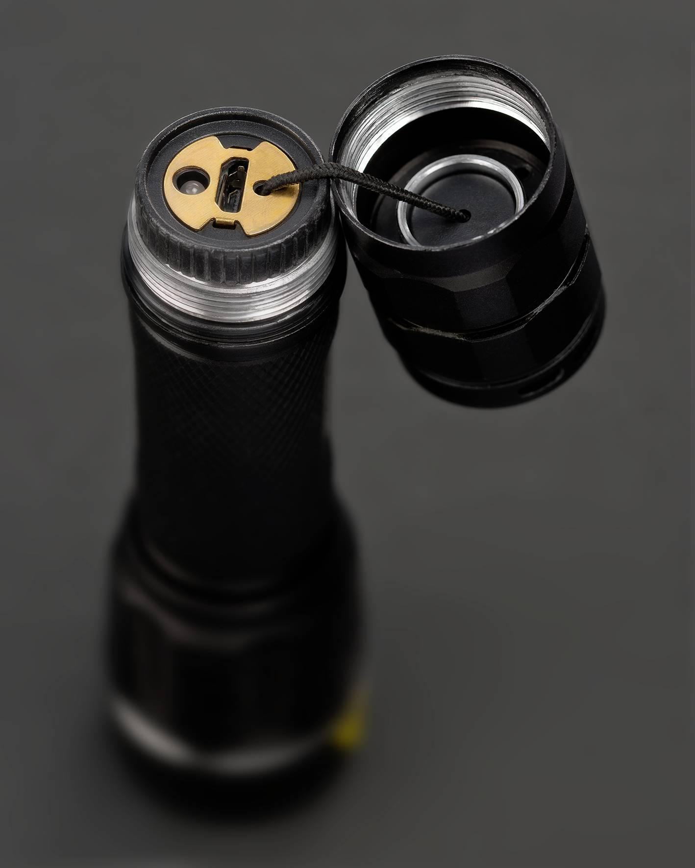 An open torch with its base removed reveals the battery connection with a cable linked to a gold-coloured contact.
