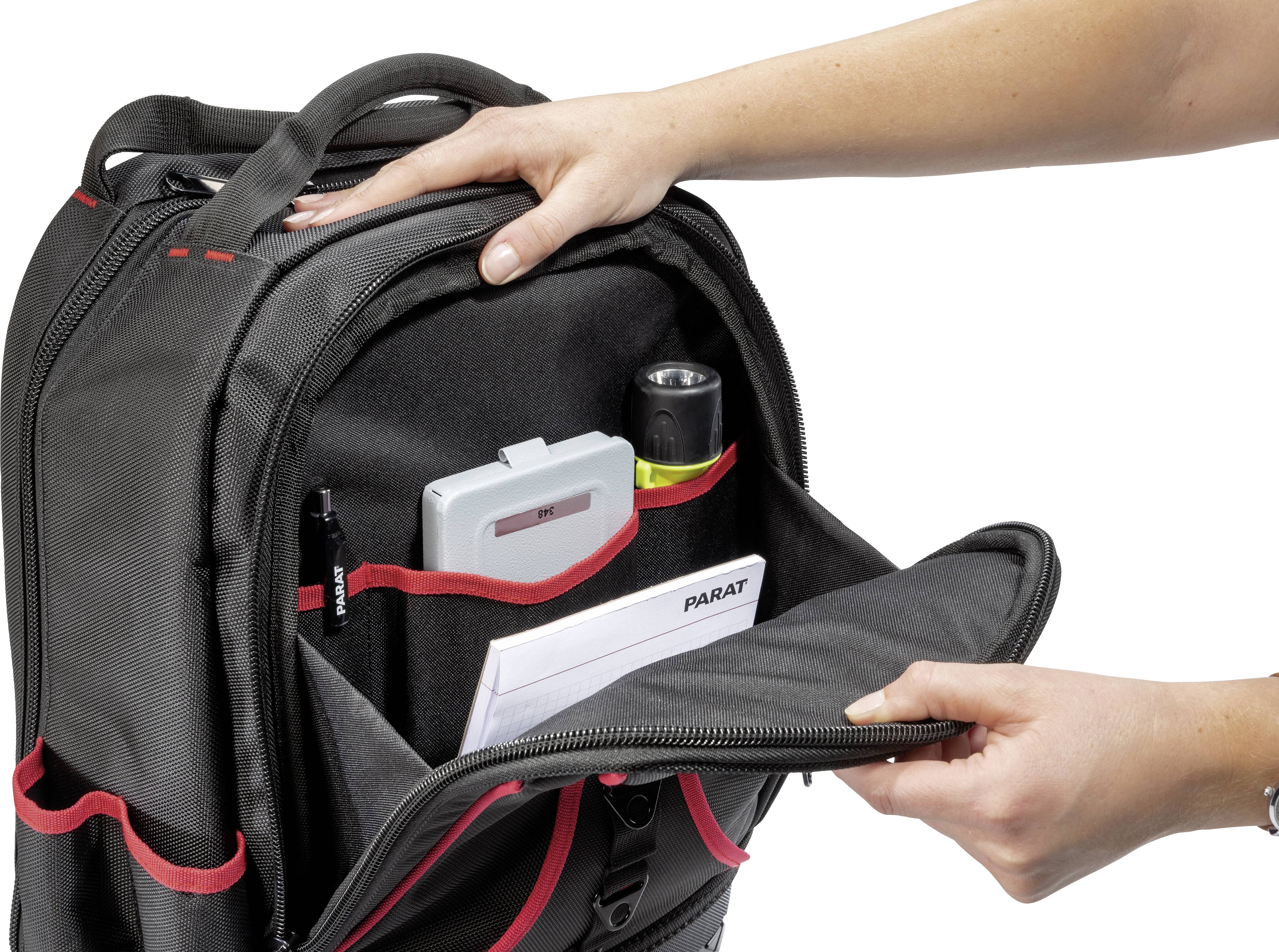 A person opens the front part of a black rucksack with red accents, revealing pockets and filled compartments.