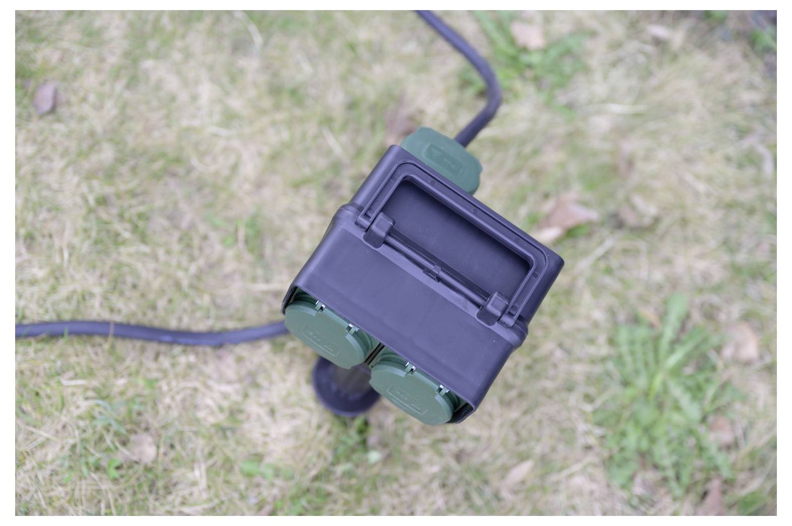 Close-up of a black and green outdoor electrical device on a cable, lying on grass.