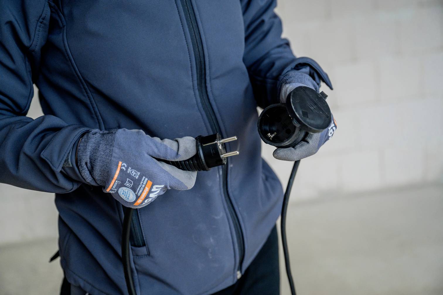 A person in a blue jacket is holding a plug and a socket in their hands, ready to connect them.
