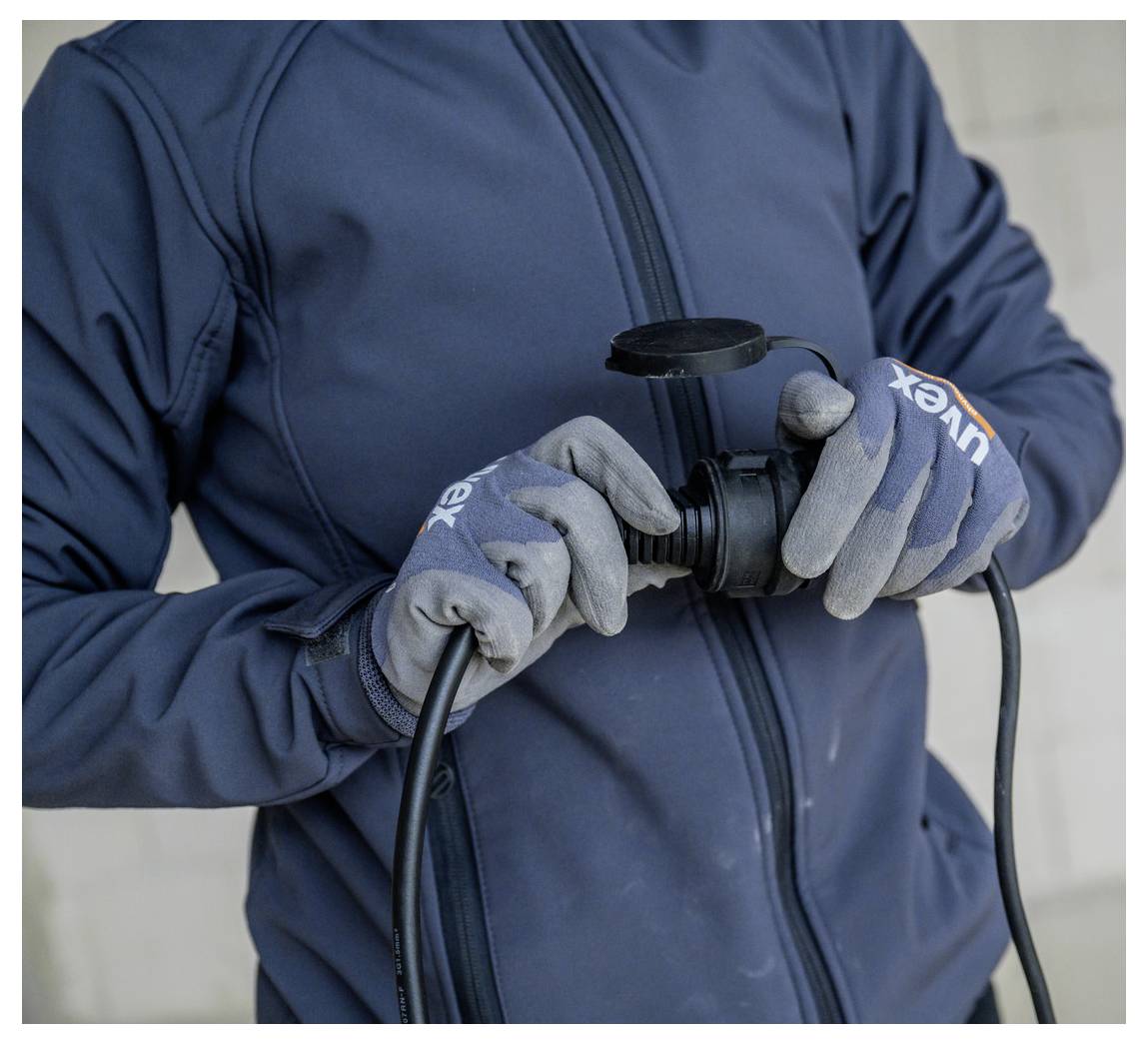 Gloved person holding and inspecting a black power cord or cable connector against a plain wall.