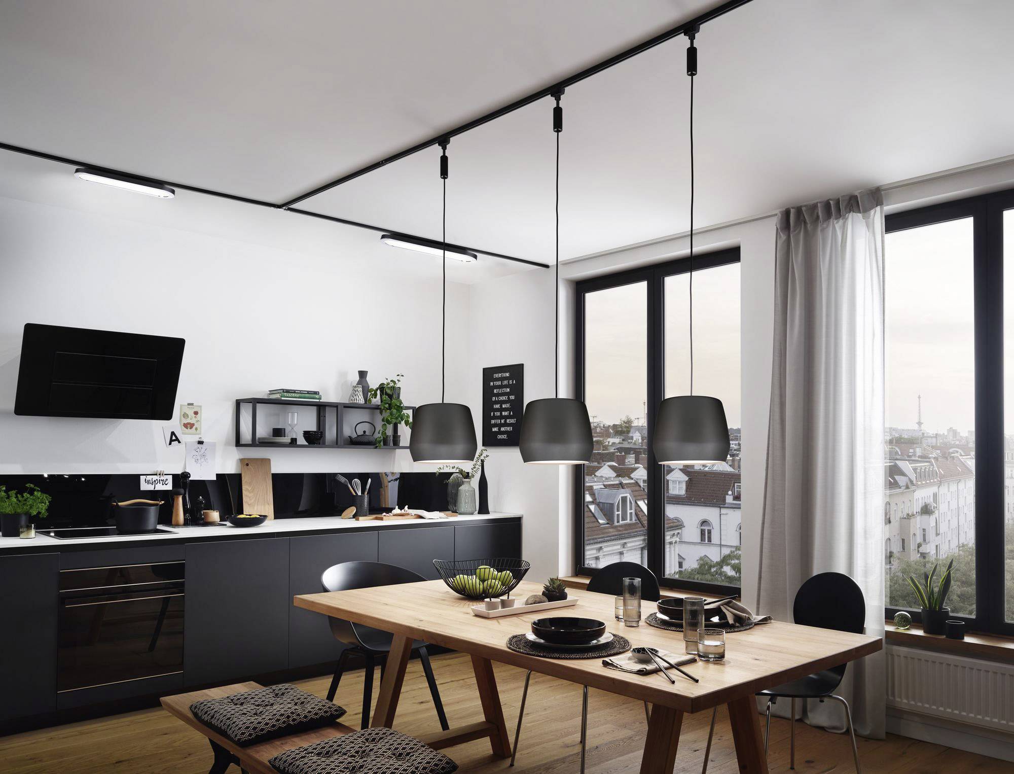 A modern living room with kitchen, wooden table, black chairs and pendant lights. Large windows offer a view of the city.