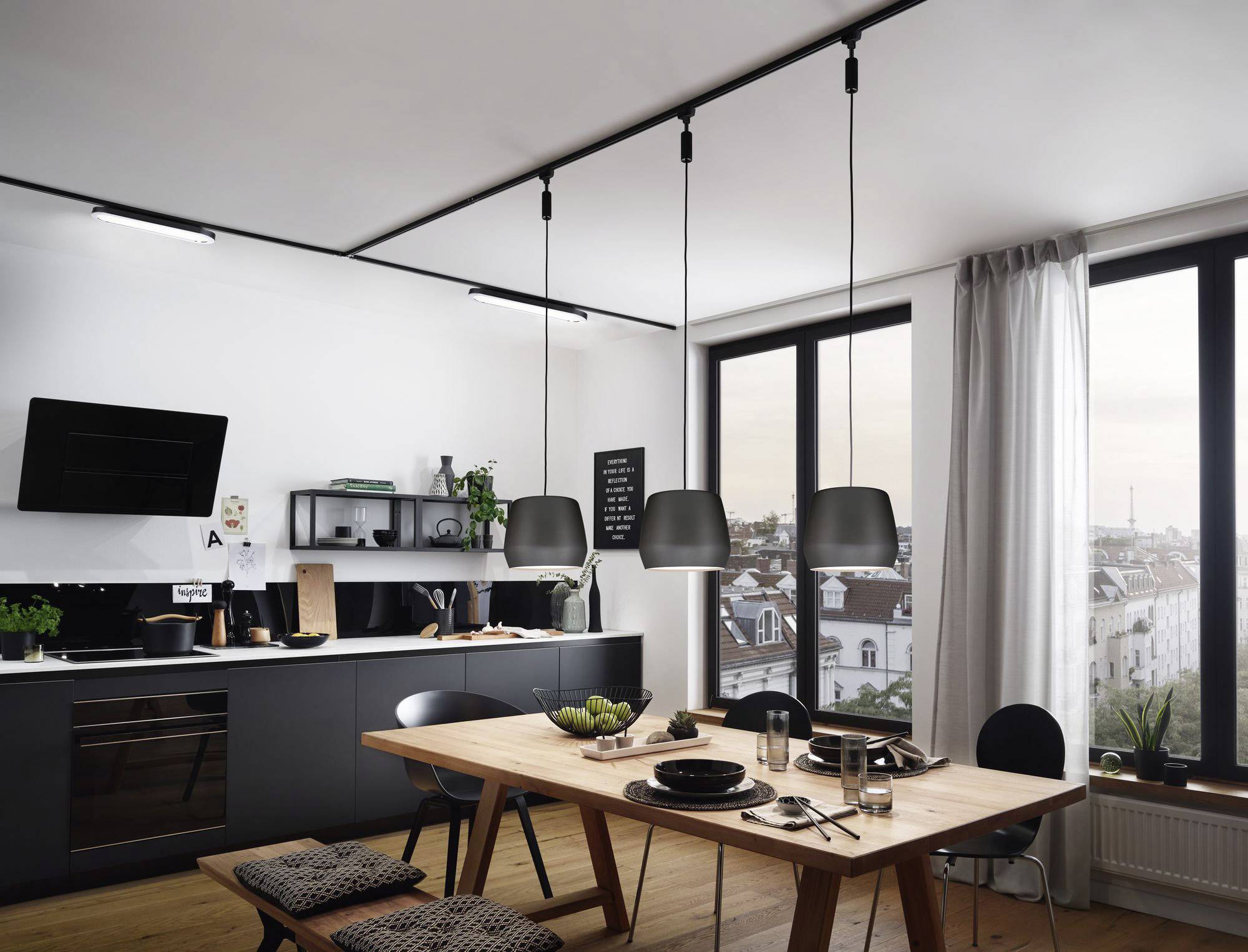 Modern kitchen with a wooden table, chairs and pendant lights. Large windows reveal a city view. Simple, stylish interior.