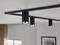 Black, cylindrical ceiling spotlights on a track in a modern room; illuminating the area beneath them.