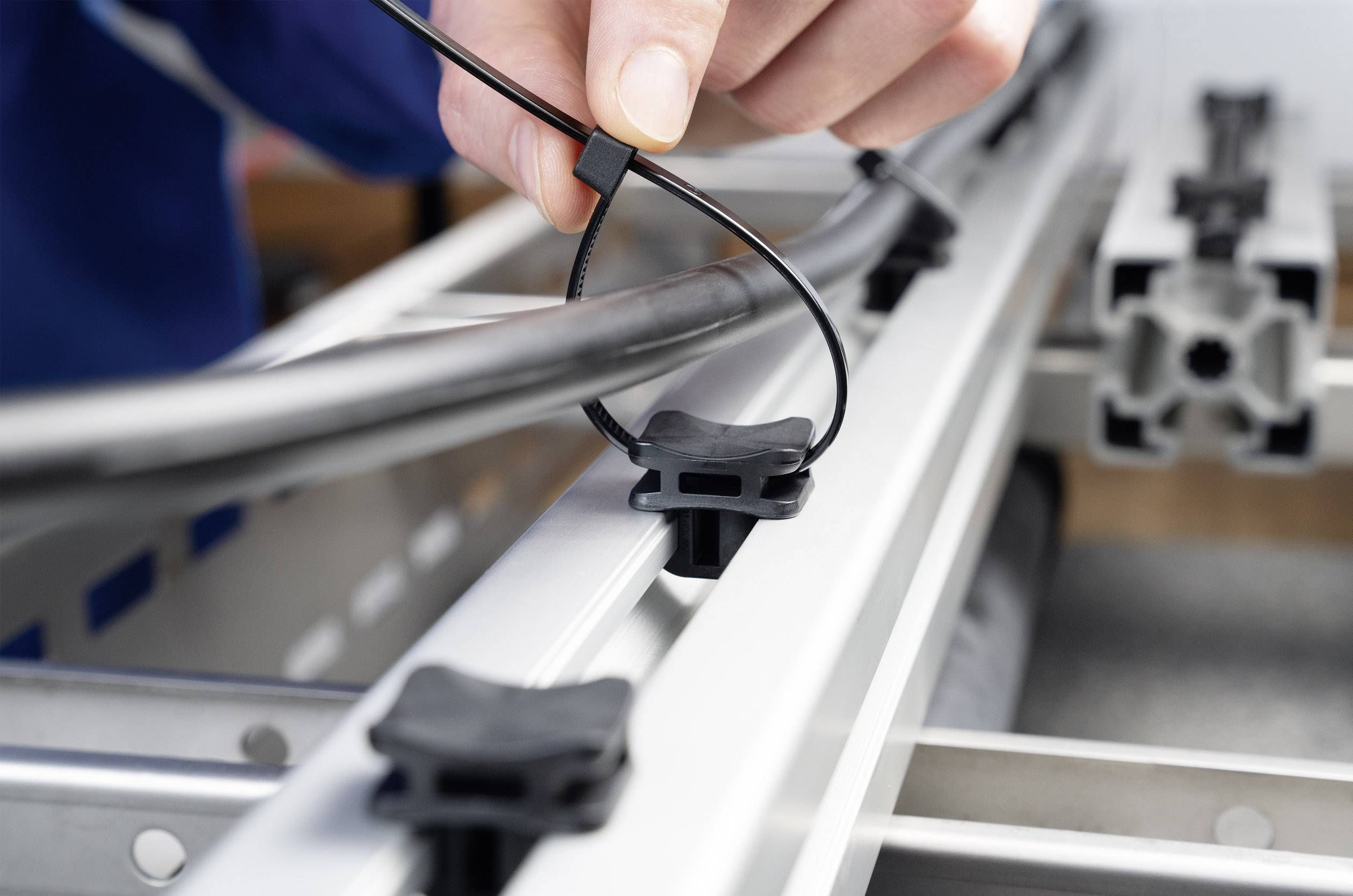 A person is securing a cable to a metal structure with a cable tie.