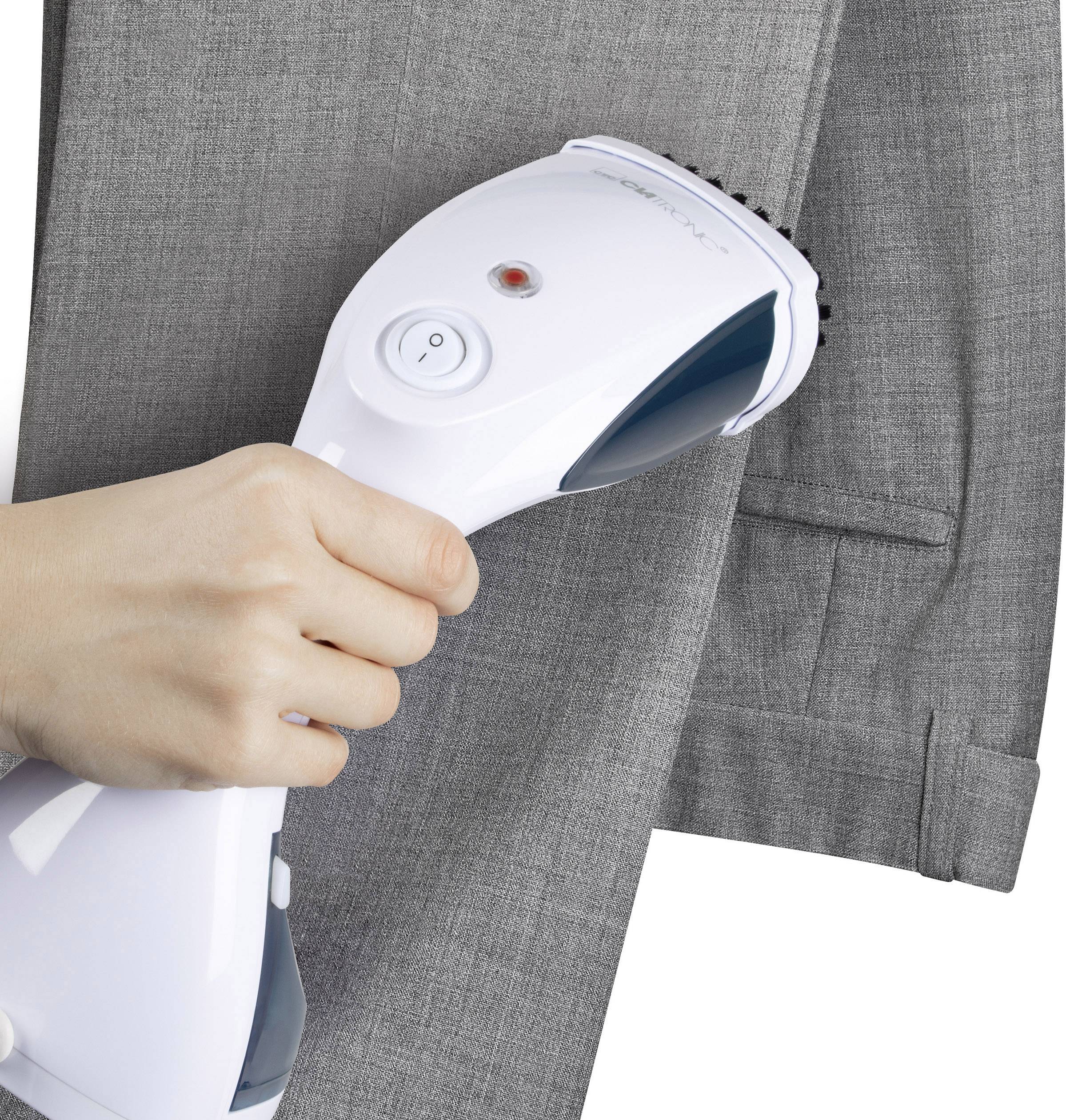A hand holds a steam iron over a grey blazer. The steam iron smooths out the creases in the fabric of the blazer.
