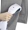 A hand holds a steam iron over a grey blazer. The steam iron smooths out the creases in the fabric of the blazer.