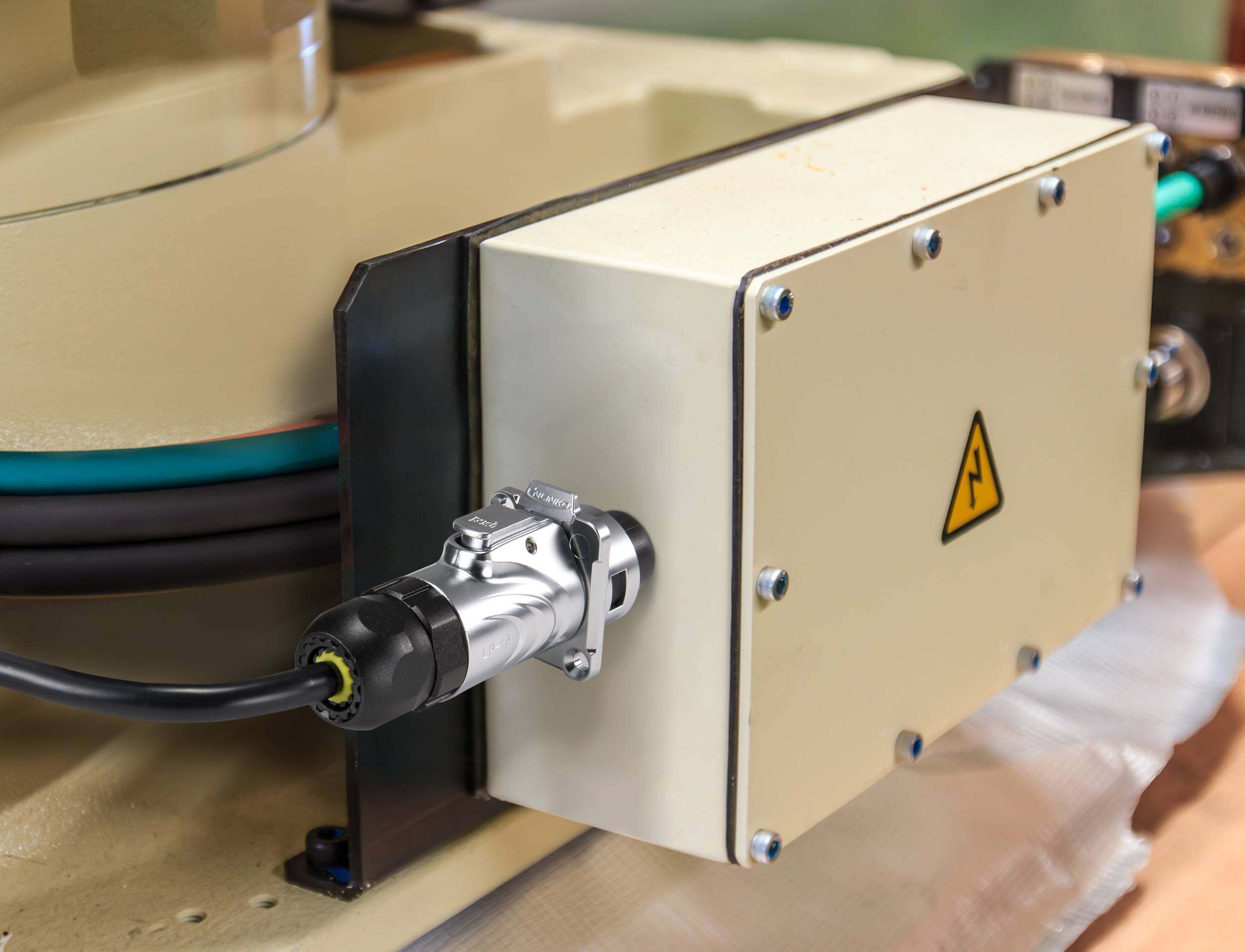 An electrical enclosure with a high-voltage warning symbol, mounted on a machine or device, connected with a cable.