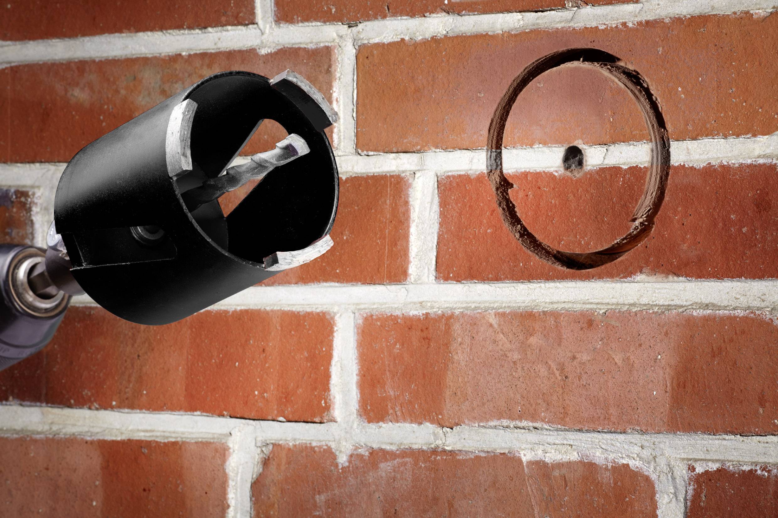 A drill with a hole saw is drilling a circular hole in a brick wall.