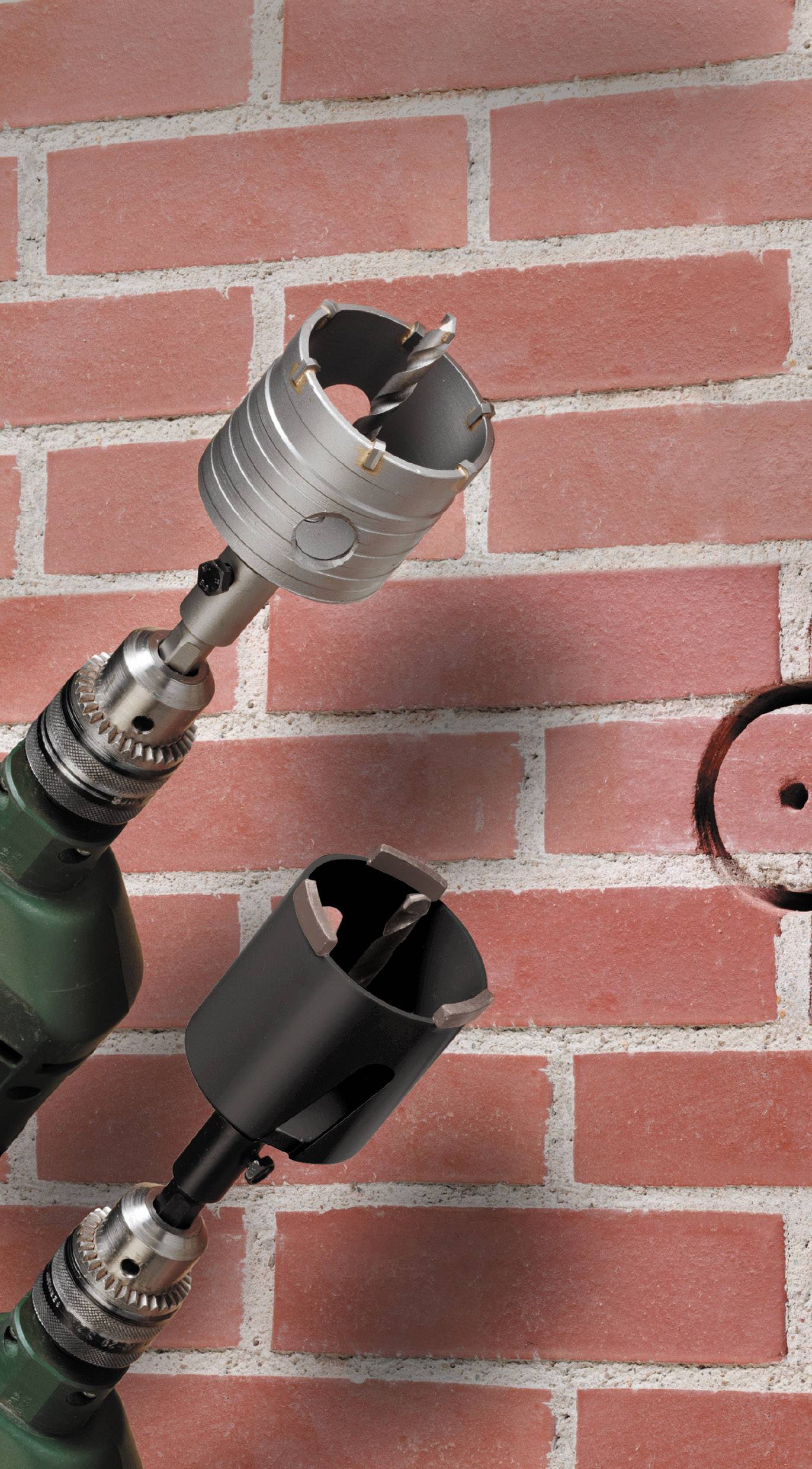 Drill with two different attachments in front of a red brick wall. The upper attachment is silver, the lower one black.