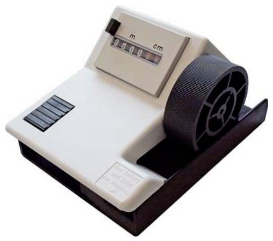 Vintage mechanical film counter device with a large black wheel and a meter window labeled m and cm.