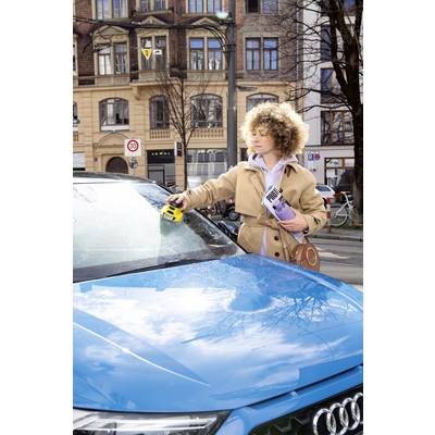 A person is cleaning the windscreen of a blue car on an urban street.